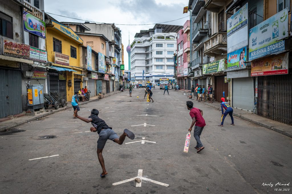 Children playing gully cricket on the bustling streets of Pettah Market.