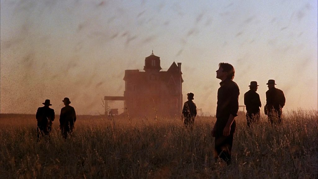Among the fields, they pause, figures shaped by the land from Days of Heaven